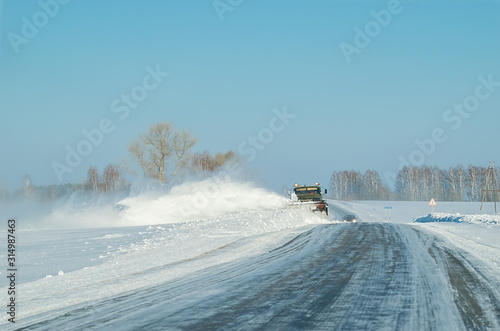 snow removal equipment, truck, winter clears the snow from the icy country road on the background of a passing car