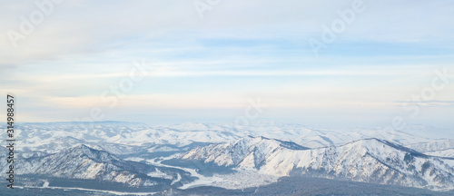Picturesque panoramic landscape in the Altai mountains with snow-capped peaks under a blue sky with clouds in winter. White snow and calm.