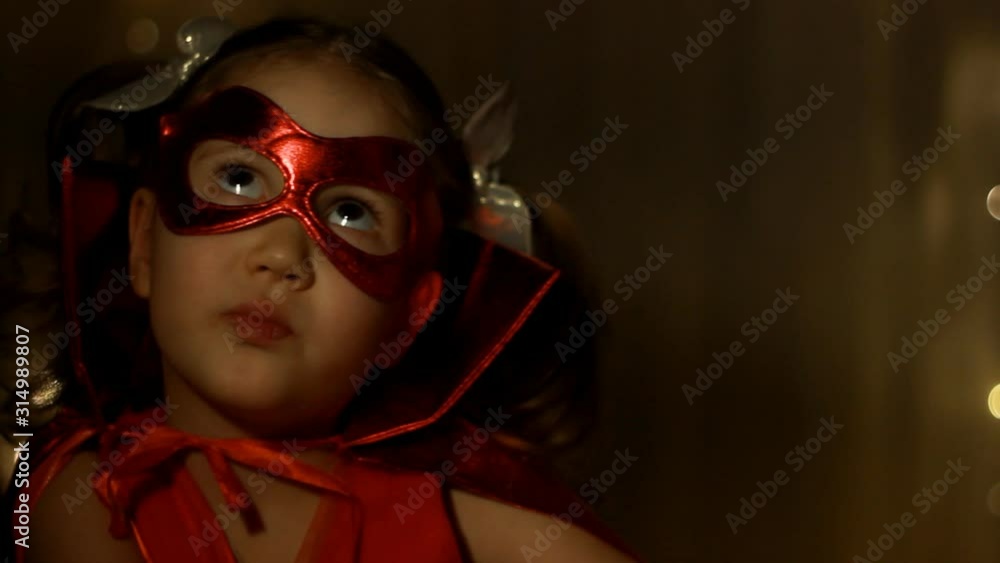 Little child girl plays superhero. Funny baby in a red raincoat playing power super hero. Superhero and power concept. Portrait close up. Selective focus. Little child girl plays superhero. Funny baby in a red raincoat playing power super hero. Superhero and power concept. Portrait close up. Selective focus.