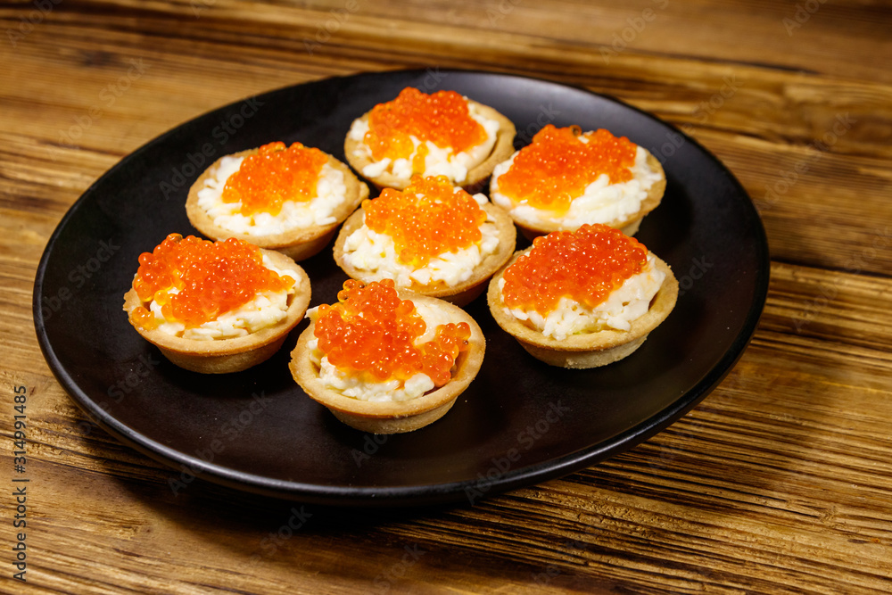 Tartlets with red caviar and soft cheese on a wooden table