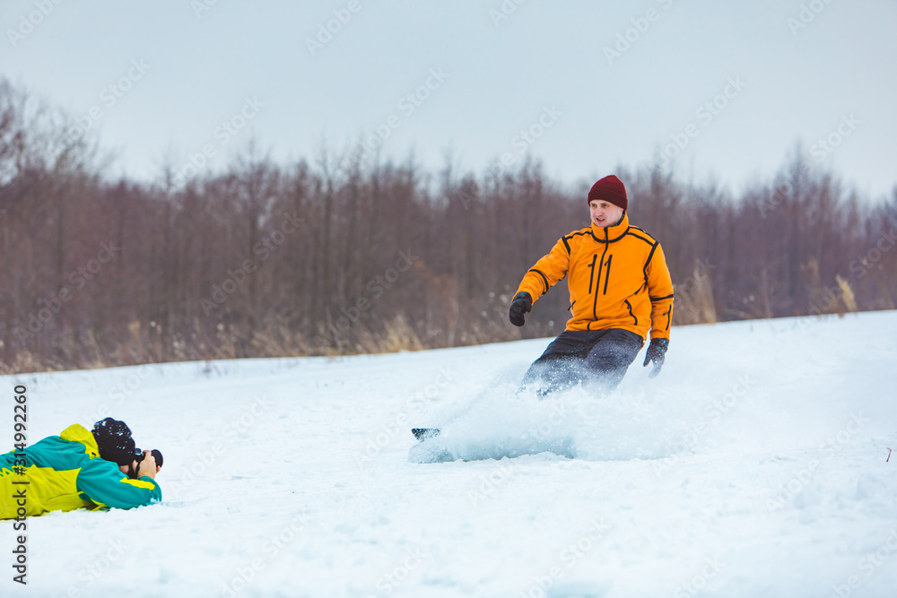 man laying on the ground and taking picture of snowboarder