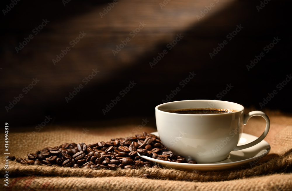 Cup of coffee and coffee beans on burlap sack on old wooden background