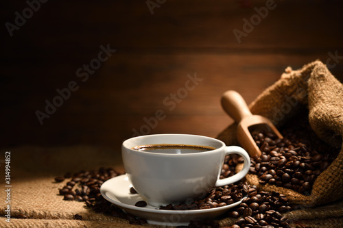 Cup of coffee with smoke and coffee beans on burlap sack on old wooden background © amenic181