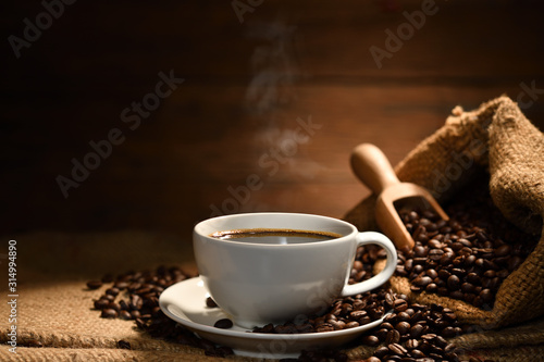 Cup of coffee with smoke and coffee beans on burlap sack on old wooden background © amenic181