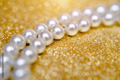 A necklace of pearls lies on a shiny gold background.