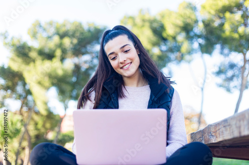 Young beautiful woman sitting outdoors while working with laptop