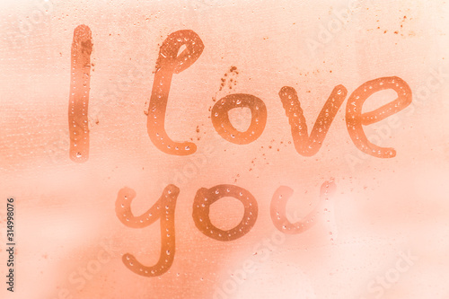 The romantic inscription I love you on the orange or pink evening or morning window glass with drops 