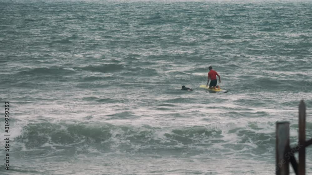 A slow motion long shot of two surfers balancing on their surfboards in the sea, on a choppy day. The waves roll over and under the surfers. A slow motion long shot of two surfers balancing on their surfboards in the sea, on a choppy day. The waves roll over and under the surfers.