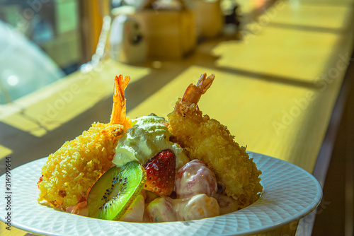 Shrimp tempura with various fresh tropical fruit salad in white bowl with blurred background, selective focus on shrimp  photo