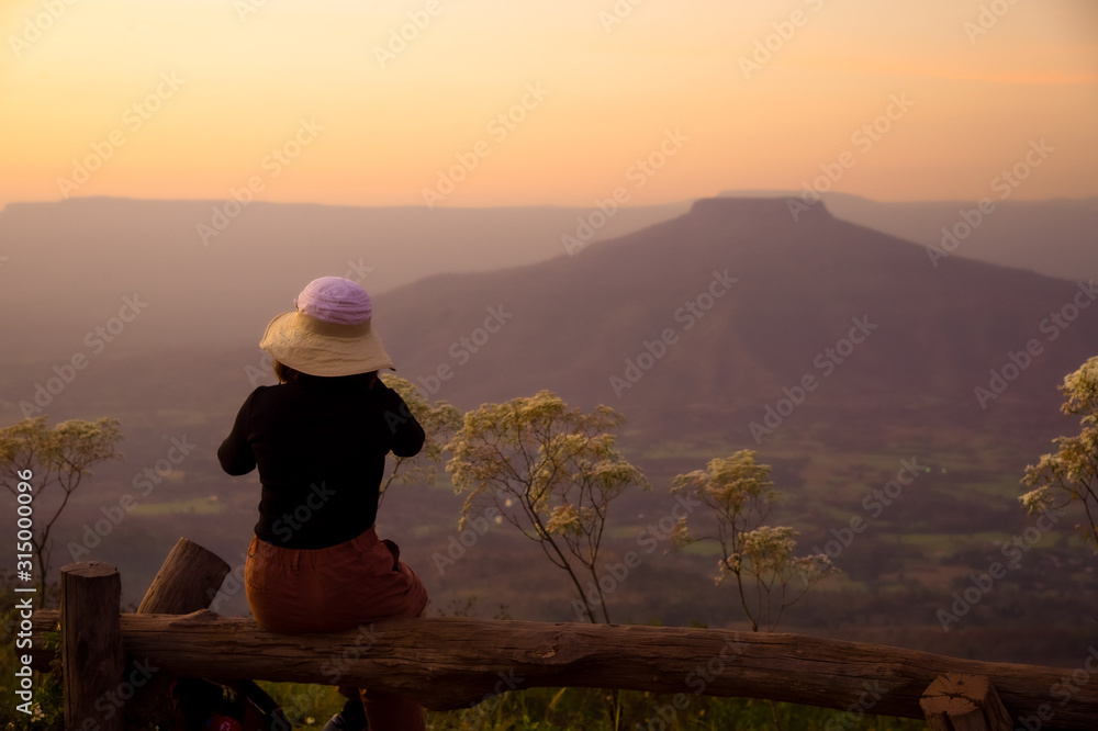 Φωτογραφία Young Asian tourist girl sitting on the wooden bench and take photo stunning amazed nature landscape of beautiful fresh morning sunrise in Thailand