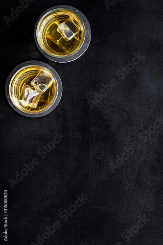 Whiskey with ice. To glasses of strong alcohol drink on black desk top-down frame copy space