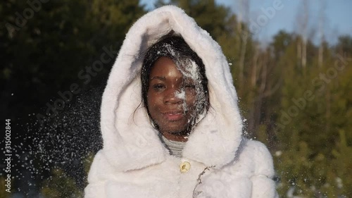 happy girl in fur hood gets snowball in black-skinned face and smiles having fun at photoshoot in forest closeup slow motion photo