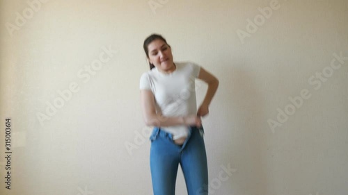 brunette struggles to pull on her jeans and can't button them.
