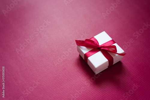 Gift box with a satin ribbon and bow on a purple background