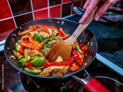Close up and selective focus of a spicy chicken and vegetable dish being cooked in a non-stick wok by an unidentifiable home chef