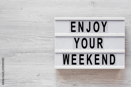 'Enjoy your weekend' words on a modern board on a white wooden background, top view. Overhead, from above, flat lay. Copy space.