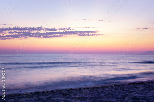 Long exposure beach landscape with purple blurred water. Pink orange horizon. Scenic seascape with sunset sky and motion blur water. Beautiful sunset sky.