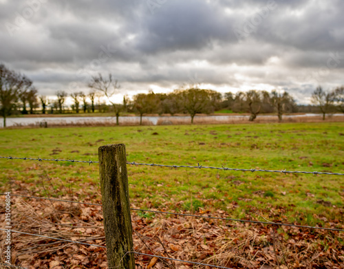 Selective focus on wooden fence post and barbed wire with a country estate lake in the distance