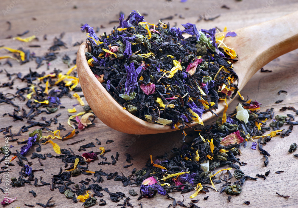 blended tea. black tea with dry flower petals and fruits. dry black tea leaves in a wooden spoon. close up - obrazy, fototapety, plakaty 