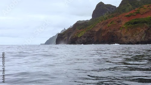 HD 120fps Hawaii Kauai Boating on the ocean pan right to left from rocky shoreline and cliffs in distance to ocean with dolphins hiding in the foreground