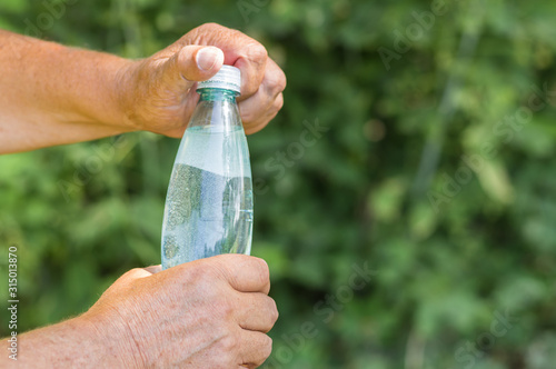 Man's hands opening bottle of mineral water against green natural background photo