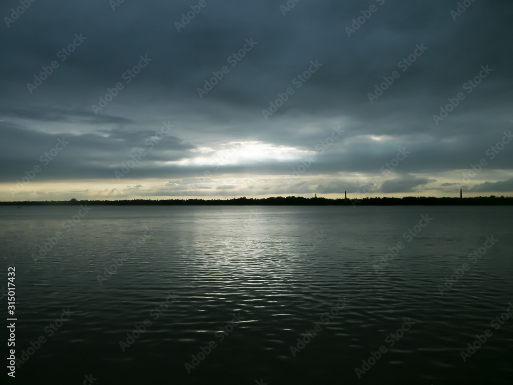 Beautiful Sun Rays of bright light shining through hole of dark clouds and illuminating lake water horizon in sunset time. Dramatic Texas sky atmosphere. Beauty in nature background.