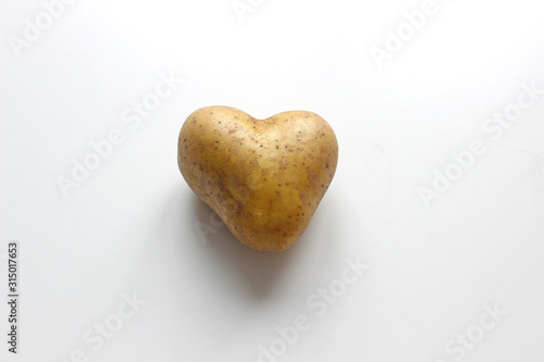 Ugly potato in the heart shape on a gray background. Funny, unnormal vegetable or food waste concept. Horizontal orientation