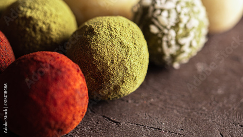 Colorful homemade truffles coated in dry beet powder, matcha tea powder, shredded cococnut on dark background. Copy space for text or design, banner. photo