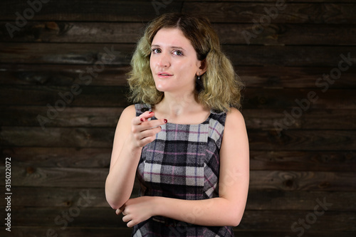 Portrait of a pretty girl with beautiful curly hair is standing in front of the camera on a wooden background. A horizontal photo concept of a cute young woman with emotions in a checkered dress.