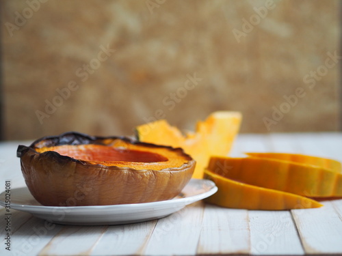 Cooking pumpkins. Home cooking, natural food for vegetarians. Traditional autumn pumpkin dishes. Grilled grilled pumpkin with spices on a background of raw pumpkin on a white wooden table.