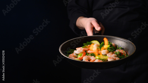 Seafood, shrimp chef cook with vegetables and fire on a black background.Banner, Delicious and healthy vegan cuisine