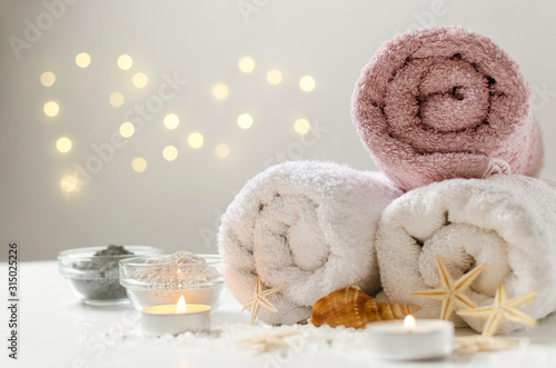 Peaceful atmosphere at the spa salon. Glass bowls of clay for body care, towels, candles and sea salt on the white surface against lights on the wall