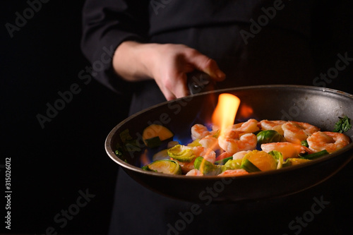 Professional cook cooks shrimps with vegetables on fire. Cooking seafood