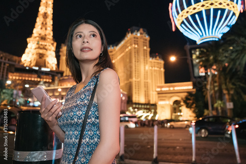 Canvas Print Young beautiful girl tourist looking at mobile phone at night modern city