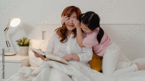 Asian grandmother relax at home. Senior Chinese, grandma happy relax with young granddaughter girl enjoy close her eyes surprise playing together lying on bed in bedroom at home at night concept.