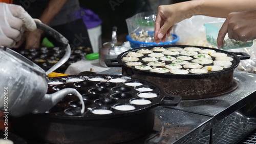 Traditional Thai desserts. The female vendor is dressing up on the mold. Kanom Krok in Thailand 