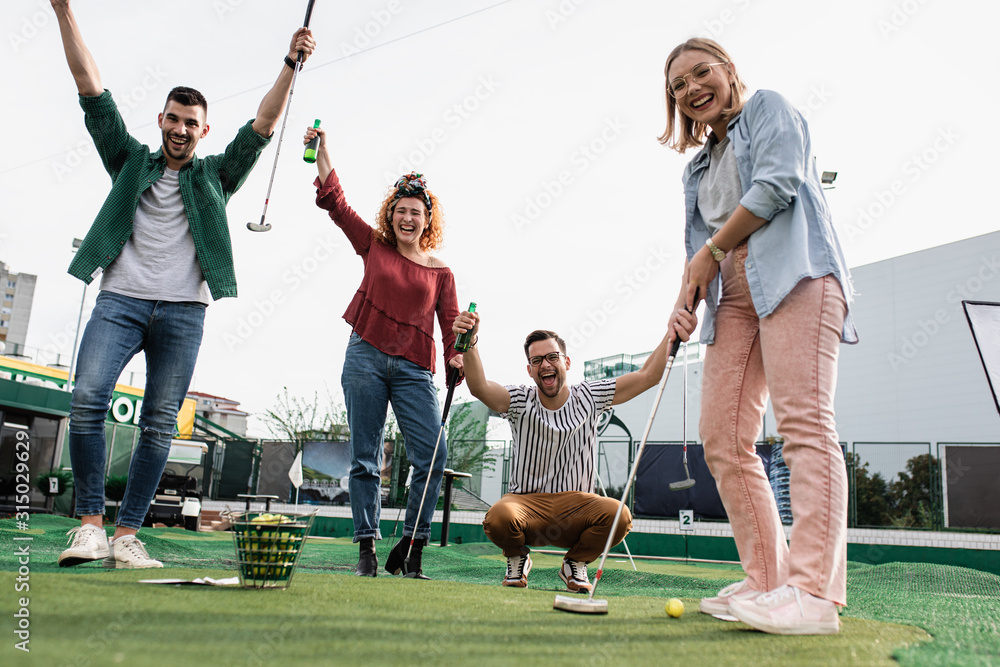 Group of smiling friends enjoying together playing mini golf in the city. - obrazy, fototapety, plakaty 