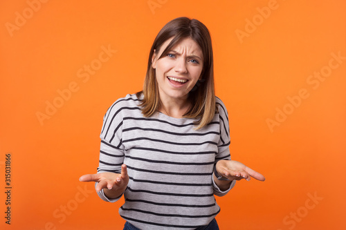 Fototapeta What do you want? Portrait of confused annoyed woman with brown hair in long sleeve shirt raising arms, asking and having no idea what happening