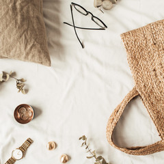 Frame with copy space made of fashion women accessories, straw bag, pillow, eucalyptus branches on white linen. Flat lay, top view blank mockup concept for social media, website, blog.