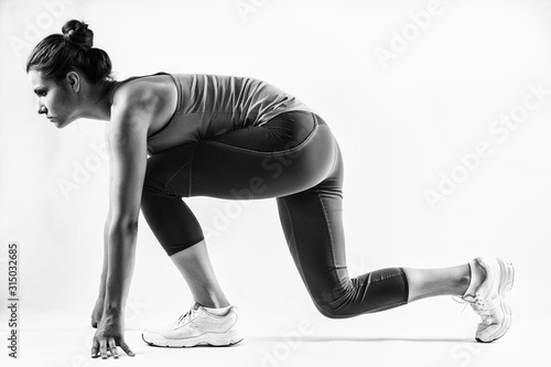 Fit female athlete ready to run over grey background. Female fitness model preparing for a sprint
