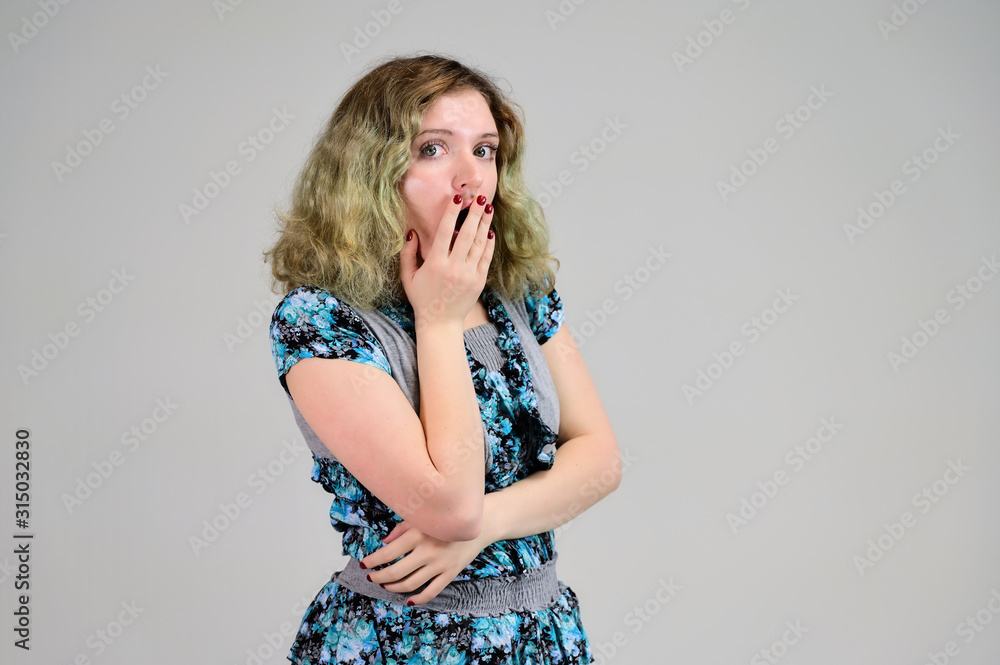 Fototapeta premium Concept horizontal photo of a young woman with emotions in a turquoise dress stands in front of the camera on a white background. Portrait of a student girl with beautiful magnificent hair.