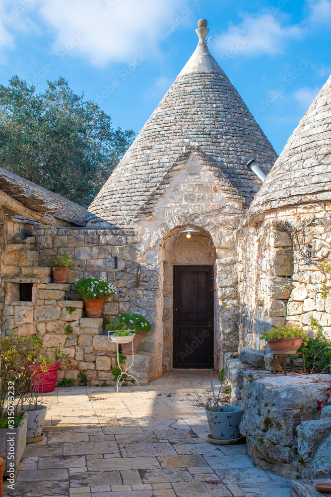 Group of Trulli with garden, traditional old houses and old stone wall in Puglia, Italy, Europe, vertical