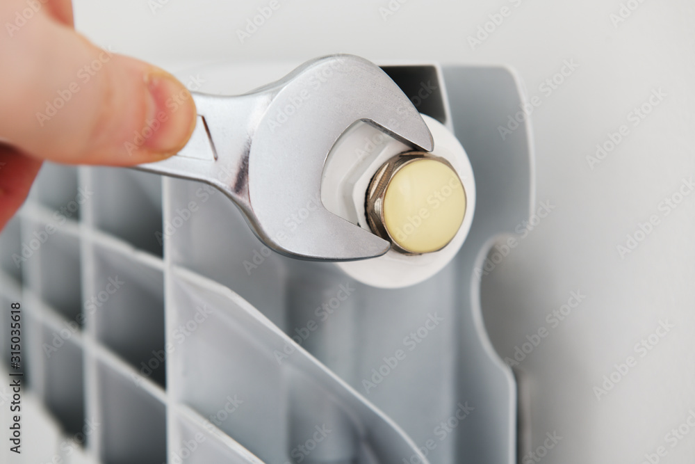 Worker hands repairing radiator with wrench. Close-up.Removing air from the radiator and fixing a heating problem.Dismantling and repair of a heating radiator in a house, apartment.Heating off. Worker hands repairing radiator with wrench. Close-up.Removing air from the radiator and fixing a heating problem.Dismantling and repair of a heating radiator in a house, apartment.Heating off.