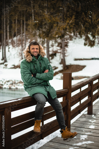 Happy bearded man in a green jacket walking in a forrest, outdoor, outfit, shoes, winter look, adventure, hiking