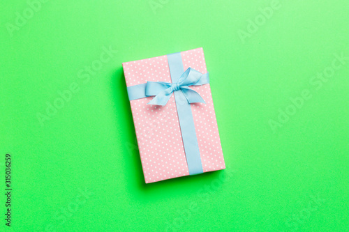 wrapped Christmas or other holiday handmade present in paper with blue ribbon on green background. Present box, decoration of gift on colored table, top view with copy space © sosiukin