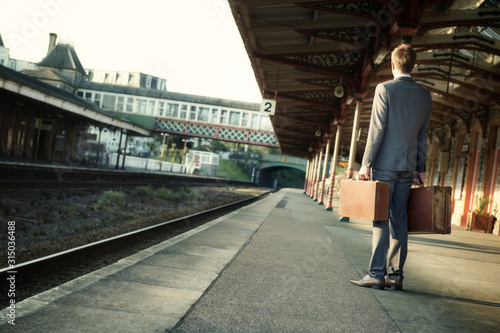 Young European businessman standing waiting outdoors on the empty platform of an old train station