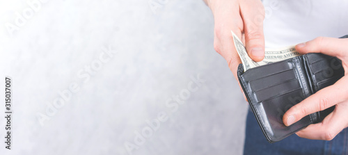 Young man holding wallet with one dollar in hands. Close up faceless photo on light background. Banner format. Financial crisis concept.