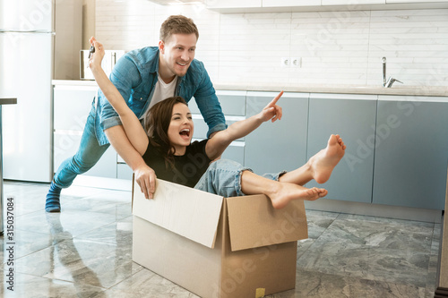 young couple husband and wife looking happy having fun while unpacking and moving in new appartment. husband carrying his wife in box on the floor photo