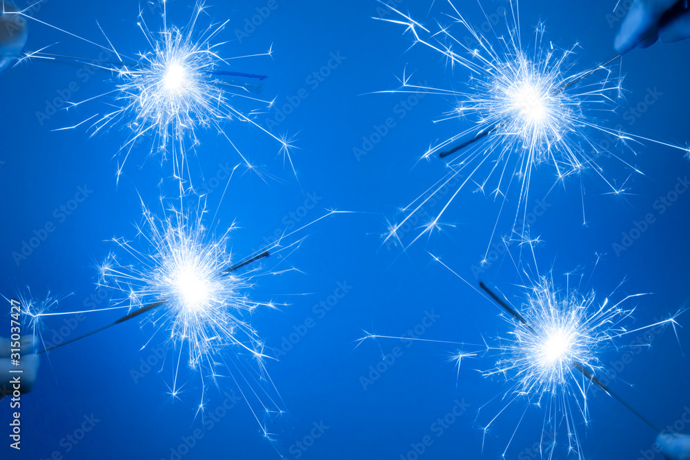 Close up of Bright burning four sparklers in hands on a blue background.