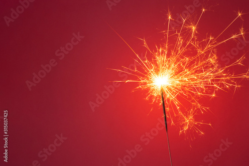 Christmas or Happy New Year party concept. Close up of Bright burning sparkler on a red background.